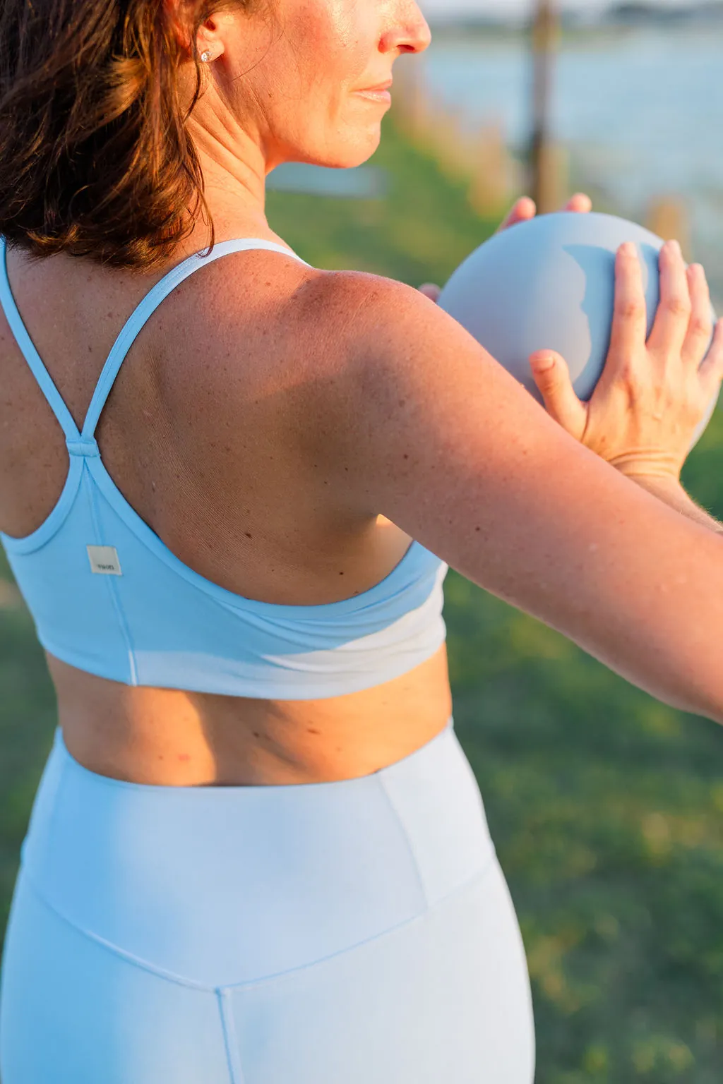 Over-the-shoulder view holding a pilates ball by the water