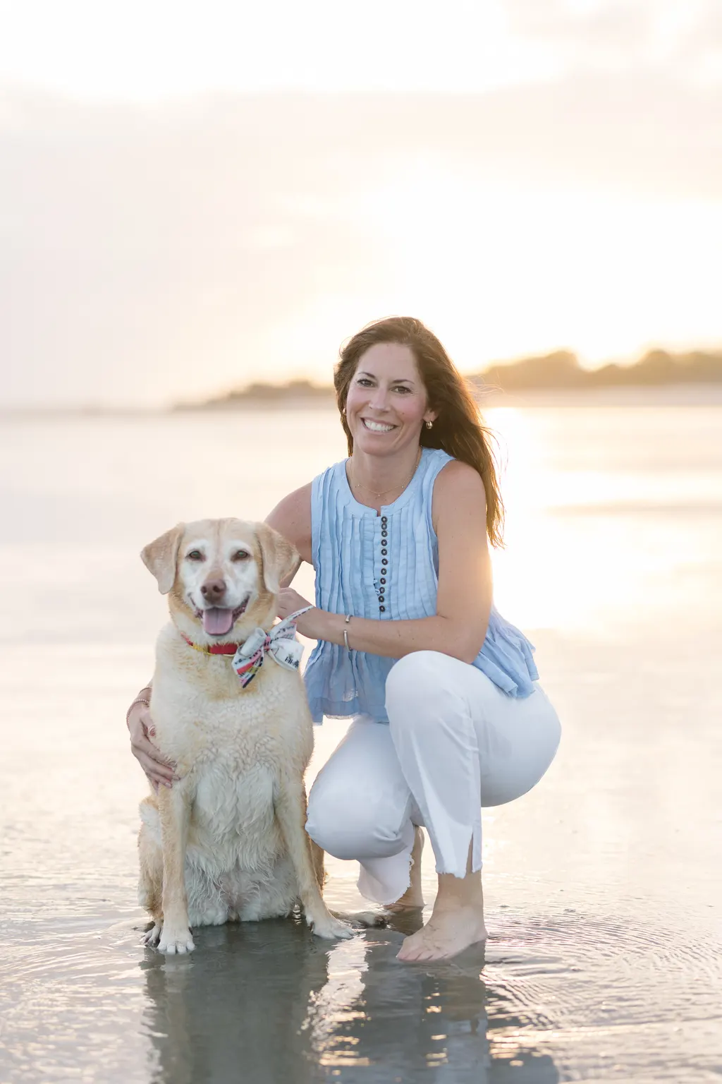 Katie kneeling on the beach at sunset with her yellow Lab, Millie