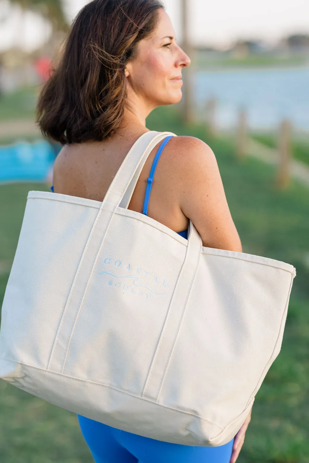 Coastal Sculpt canvas tote on the shoulder at the waterfront